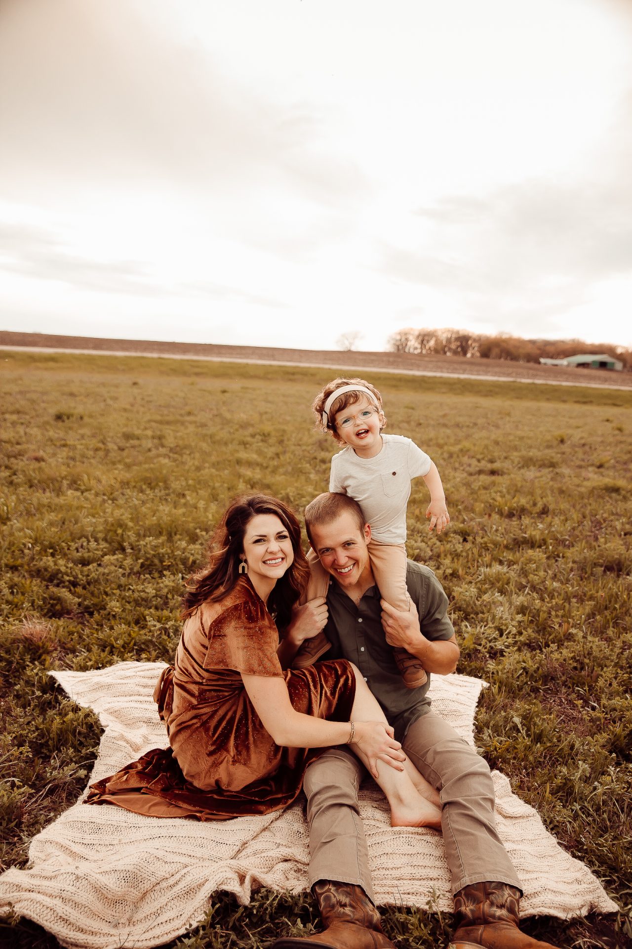 Brandon, Beth and Cooper sit in the grass smiling at the camera. Beth is an inclusion advocate with a focus on raising a deaf child.
