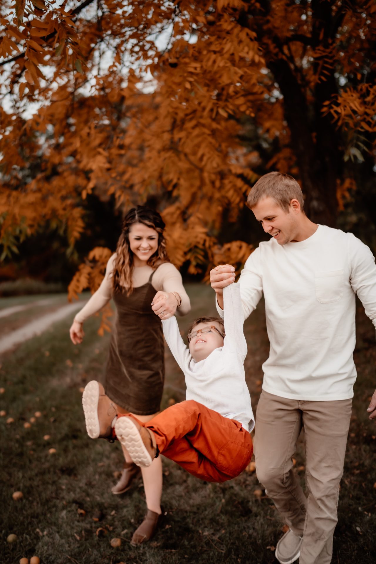 A happy moment as a young family cherishes inclusion, with the parents playfully swinging their deaf child by the arms amidst a backdrop of golden fall foliage, reminiscent of a scene from a children's book