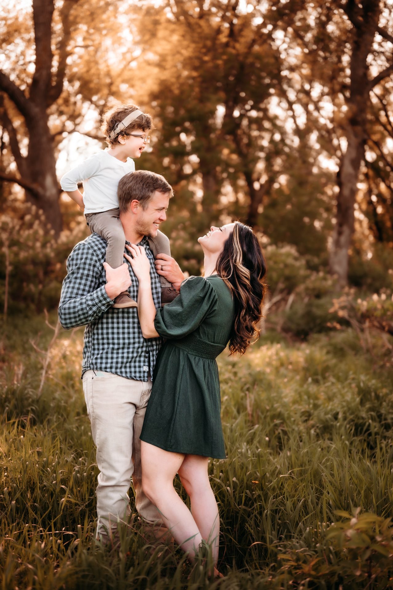 Brandon, Beth and Cooper in a grassy field. Cooper is on Brandon's shoulders. Beth is an inclusion advocate with a focus on raising a deaf child.