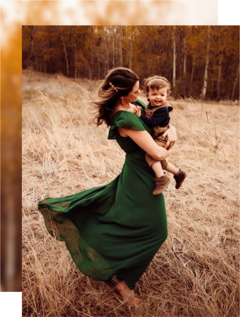 A woman in a flowing green dress spins joyfully in a field of tall grass, holding her deaf child's smiling face up to the sun. The background features autumn trees with warm golden leaves, as if nature celebrates their shared bond.